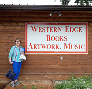 Sally by sign on the side of Western Edge Books, Artwork, and Music